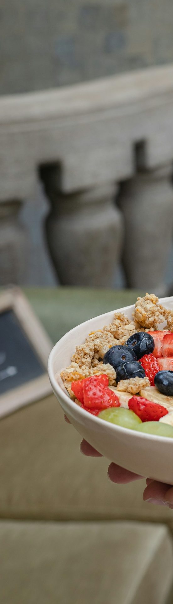 Schüssel mit Joghurt, Granola und frischen Beeren sowie geschnittenem Obst.