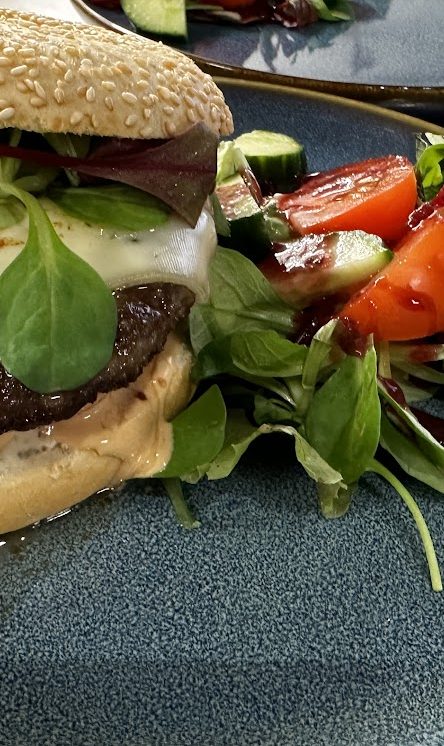 Ein saftiger Burger mit Käse, frischen Salat und einer Seite aus Tomaten und Gurken.